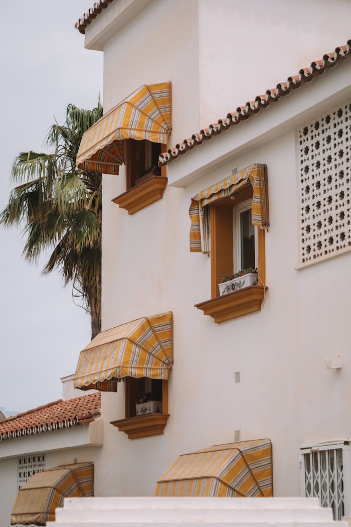 Exterior view of a classic Mediterranean building in Málaga with striped awnings and palm trees.