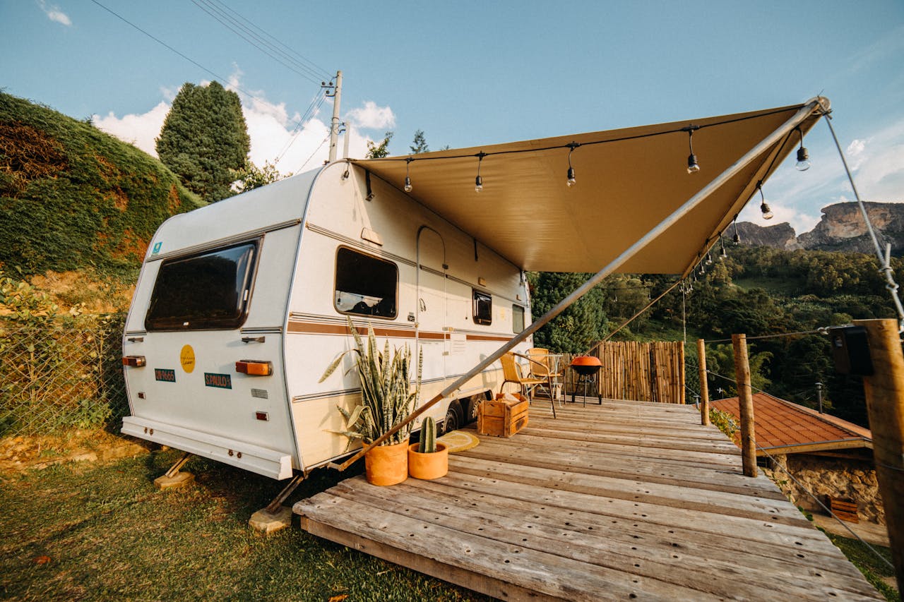 Cozy caravan camping with a wooden terrace and potted plants overlooking a scenic landscape.