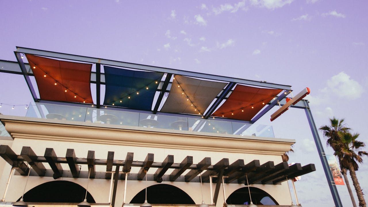 A modern rooftop terrace with colorful awnings and string lights, seen from a low angle.